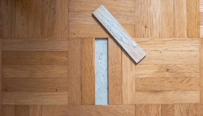 Unglued or unstuck wooden tile from an old apartment parquet floor. Visible ciment glue on the back side, top view, no people