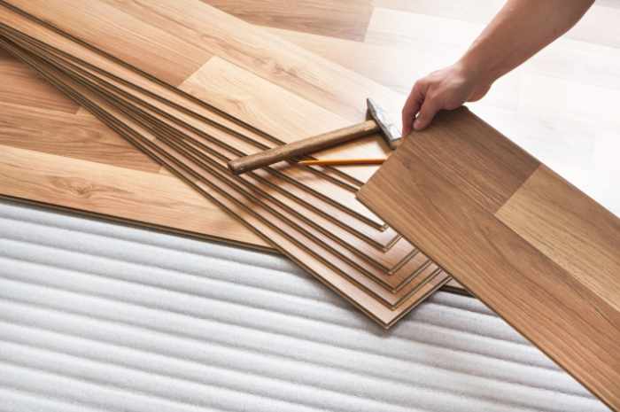 Installing laminated floor, detail on man hands holding wooden tile, over white foam base layer
